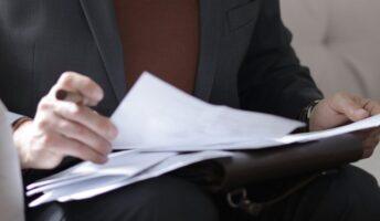 person sits on a couch while holding a paper contract and pen