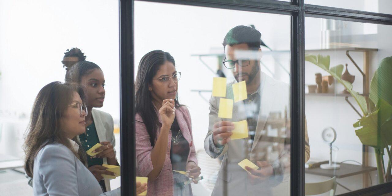 a diverse group of young people placing sticky notes on a glass wall
