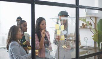a diverse group of young people placing sticky notes on a glass wall