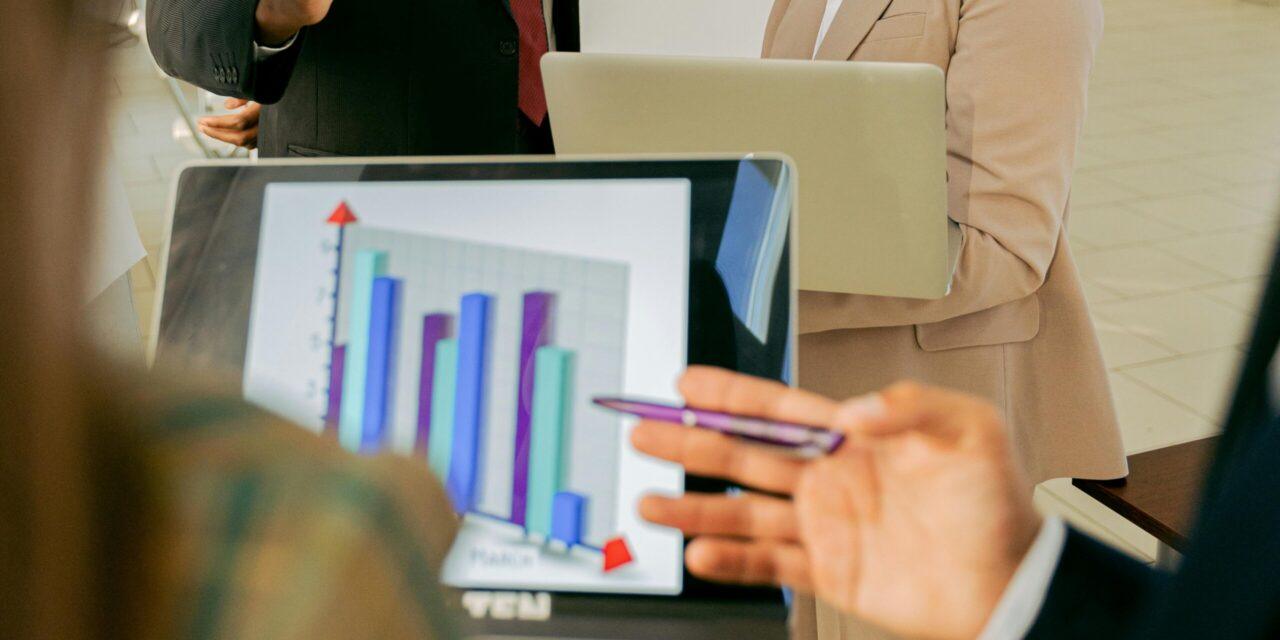 Two coworkers face a laptop to view a blue and purple bar chart that shows business growth.