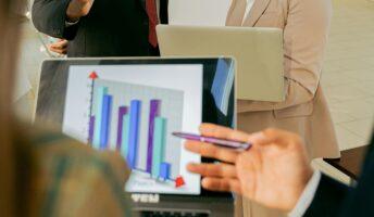 Two coworkers face a laptop to view a blue and purple bar chart that shows business growth.