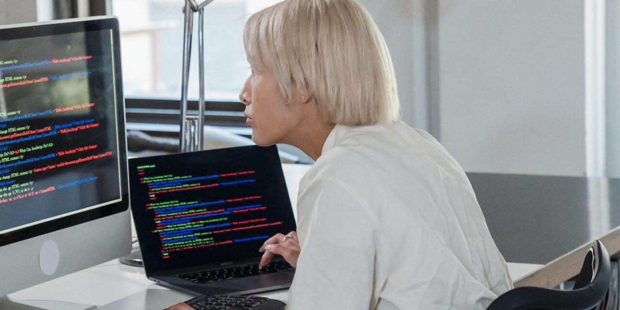 An IT worker sits in front of two computer monitors working on code