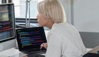 An IT worker sits in front of two computer monitors working on code
