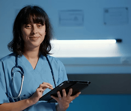 Smiling nurse in blue scrubs with a stethoscope holding a tablet