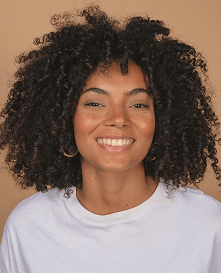 Smiling woman with curly dark hair in a white t-shirt against a tan backdrop