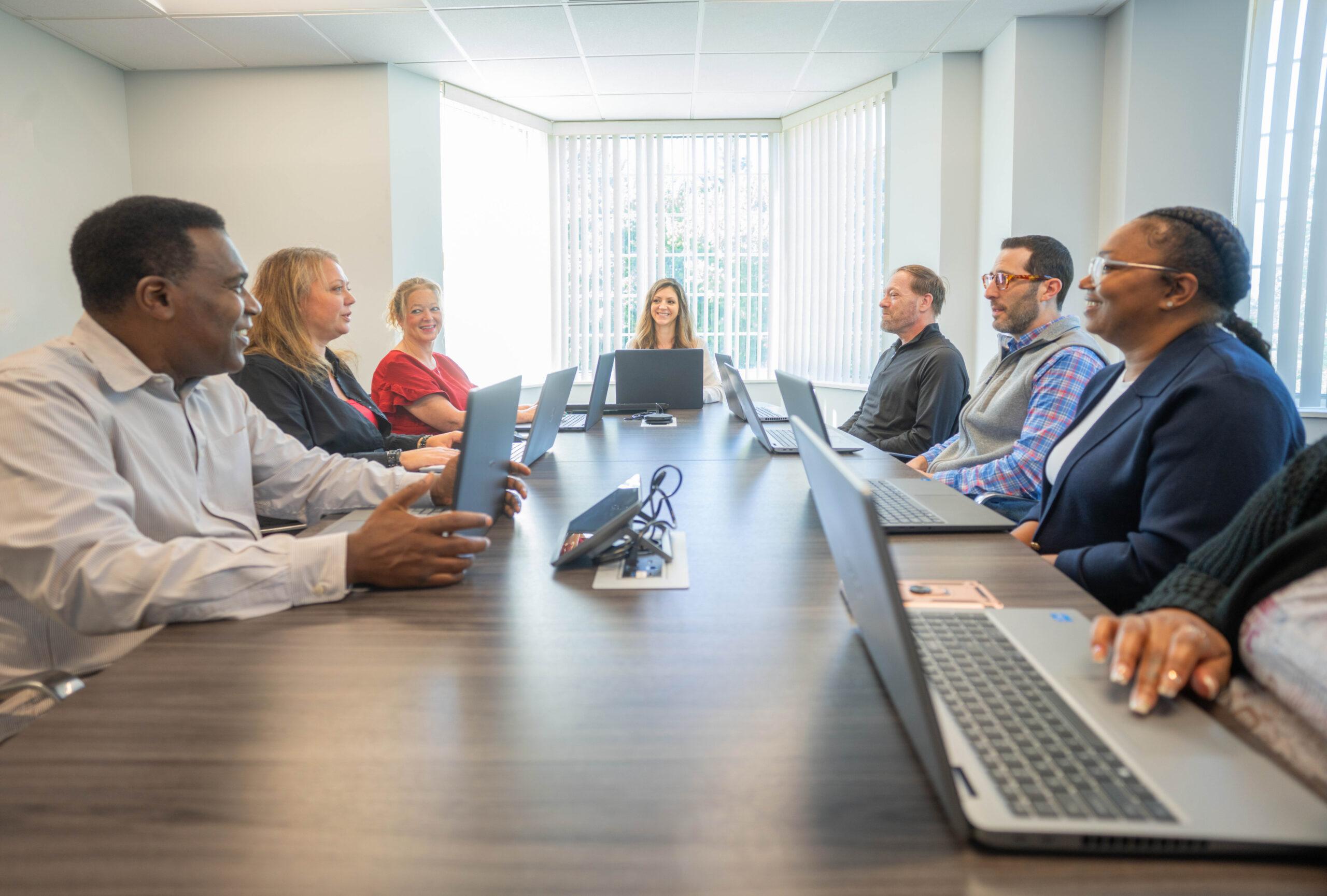 Team seated around a long conference table with laptops in a meeting