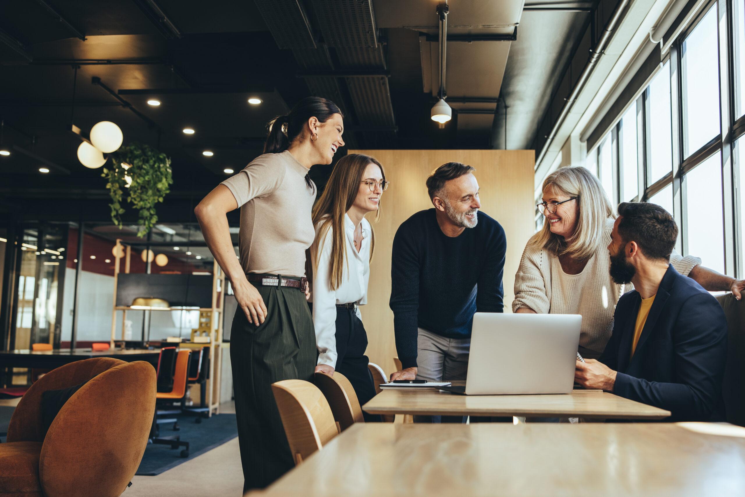 Five colleagues gathered around a laptop in a modern office