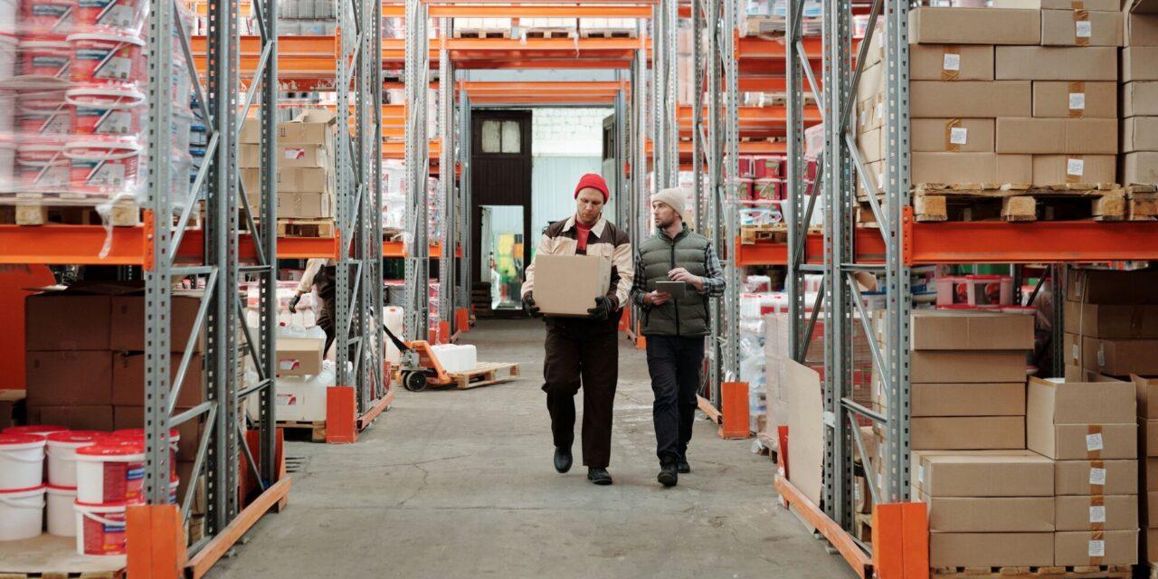 Two men walk through a warehouse full of large boxes and shelves