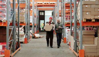 Two men walk through a warehouse full of large boxes and shelves